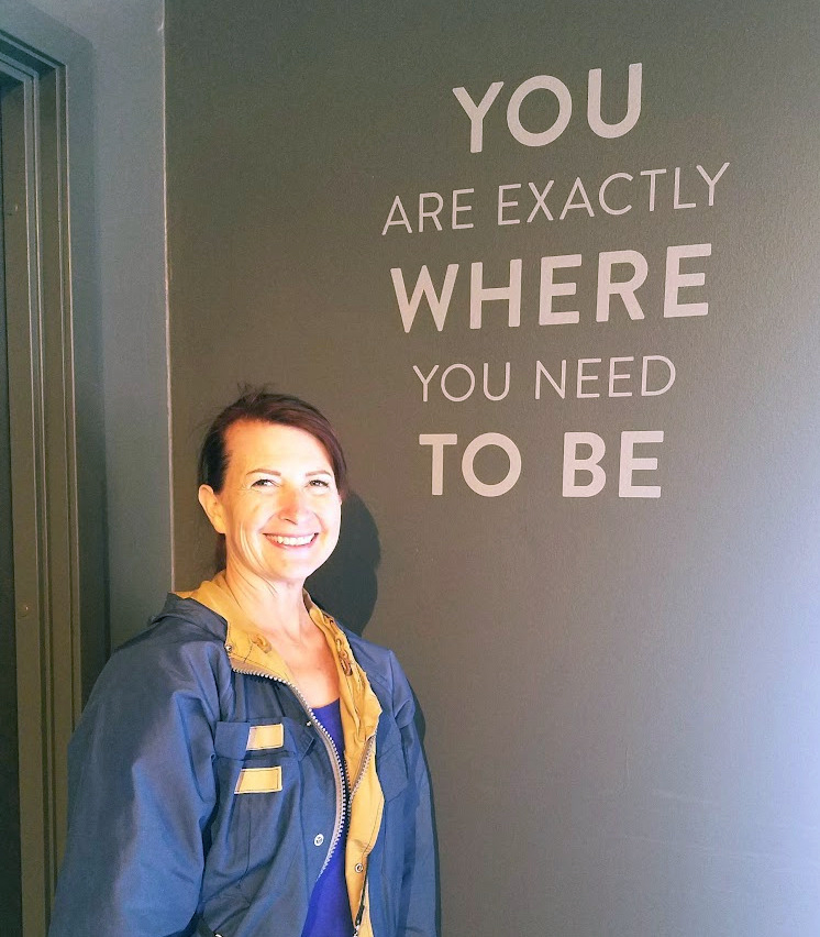 Kelly standing next to wall with the words You Are Exactly Where You Need to Be